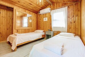 A wooden room with two beds, a nightstand, an air conditioning unit, and a window with curtains. - Base Bungalows (Kumluca)