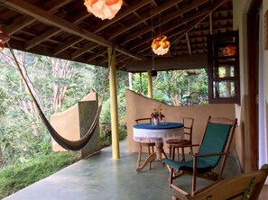 A covered outdoor seating area with a hammock, a table with chairs, and a view of the surrounding greenery. - Natural Mystic Sanctuary (Deniyaya)