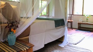 Una habitación con una cama bajo un dosel, una mesita con un jarrón de flores y una ventana con cortinas.