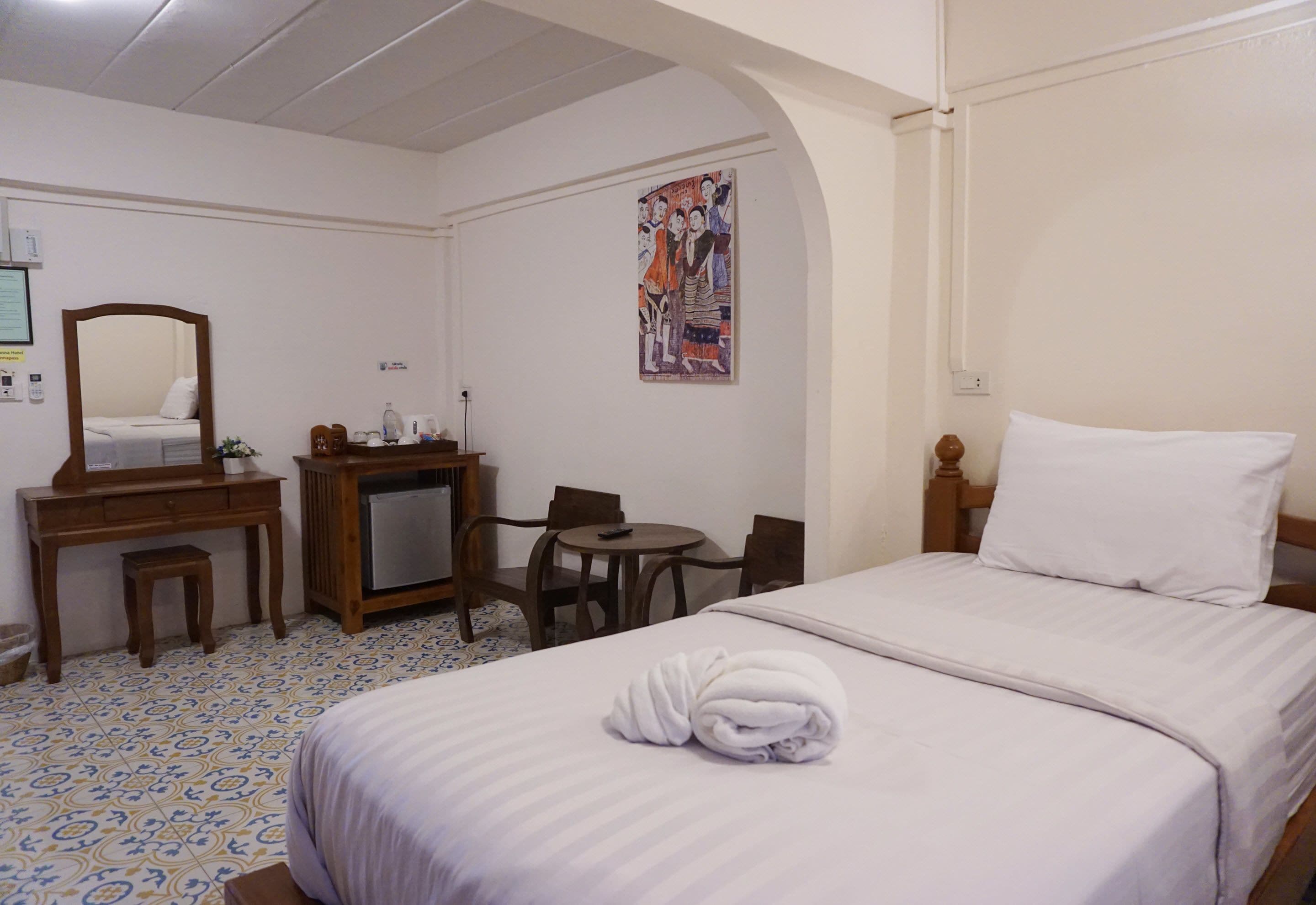 Habitación de hotel con cama, escritorio, silla, mesita, espejo y un cartel en la pared.