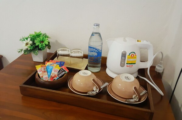 Una bandeja con cafetera, una botella de agua, una planta pequeña y un tazón de sobres de café.