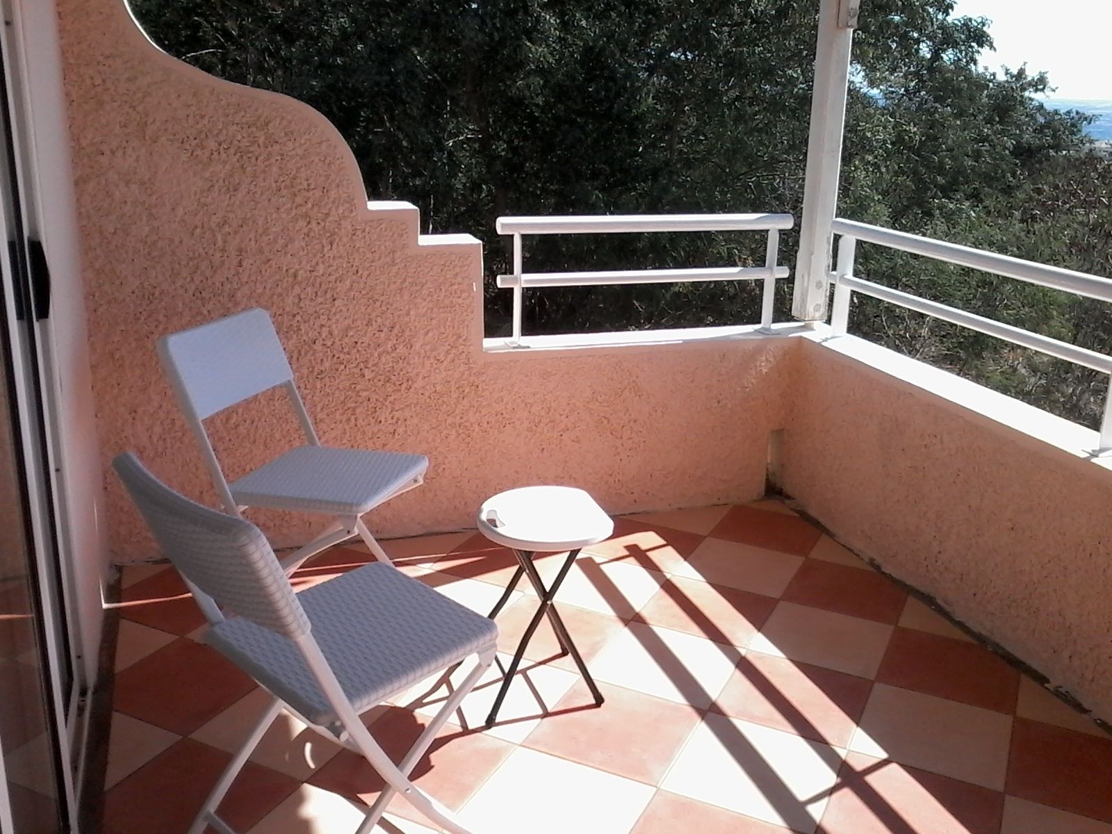Ein Balkon mit Schachbrettboden, einem weißen Stuhl und einem kleinen Tisch.