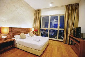 A hotel room with a large bed, a TV, a nightstand, a lamp, and a view of a cityscape through a large window.