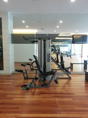 A gym with various exercise machines, wooden flooring, and a large mirror reflecting the space.