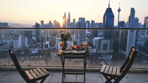 A balcony with a table set for two, overlooking a cityscape with prominent skyscrapers. - Regalia Residence @ KLCC View Sky Pool by MC (Kuala Lumpur)