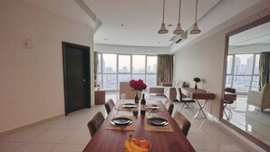 A dining area with a long wooden table set for four, a vase with flowers, and a fruit basket. - Regalia Residence @ KLCC View Sky Pool by MC (Kuala Lumpur)