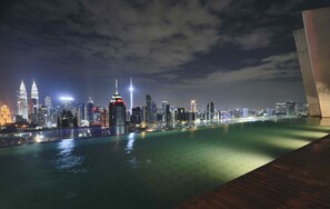 A nighttime cityscape with a prominent skyline, including two illuminated towers, over a calm body of water. - Regalia Residence @ KLCC View Sky Pool by MC (Kuala Lumpur)