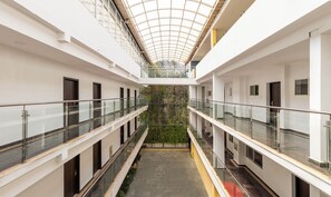 A multi-level interior with a glass balustrade, a central atrium with a green wall, and a high ceiling with a skylight. - Treebo Grand Canyon By D2V (Kochi)