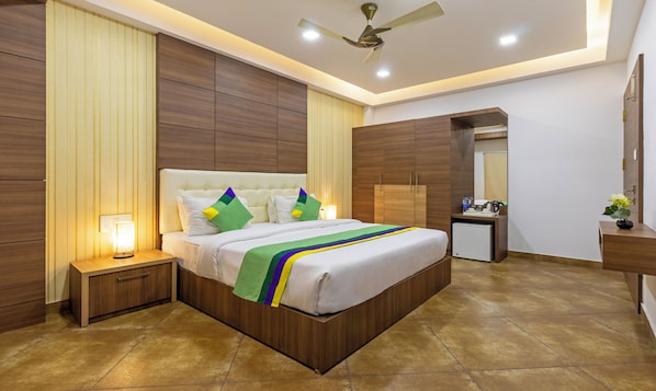 A modern hotel room with a large bed, wooden paneling on the walls, a ceiling fan, and a small side table with a lamp. - Treebo Grand Canyon By D2V (Kochi)
