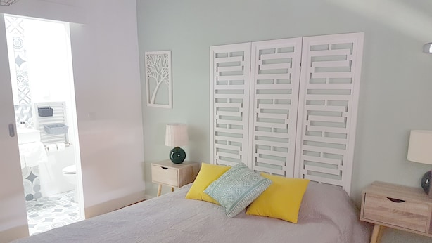 Een slaapkamer met een bed, twee nachtkastjes, een wandlamp en een deur naar een badkamer.
