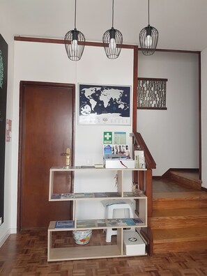 A room with a wooden floor, a bookshelf with magazines, a world map, a framed quote, and a staircase.
