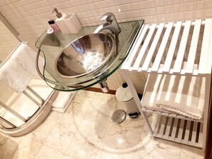 A bathroom with a glass sink, white towel rack, and a white toilet.
