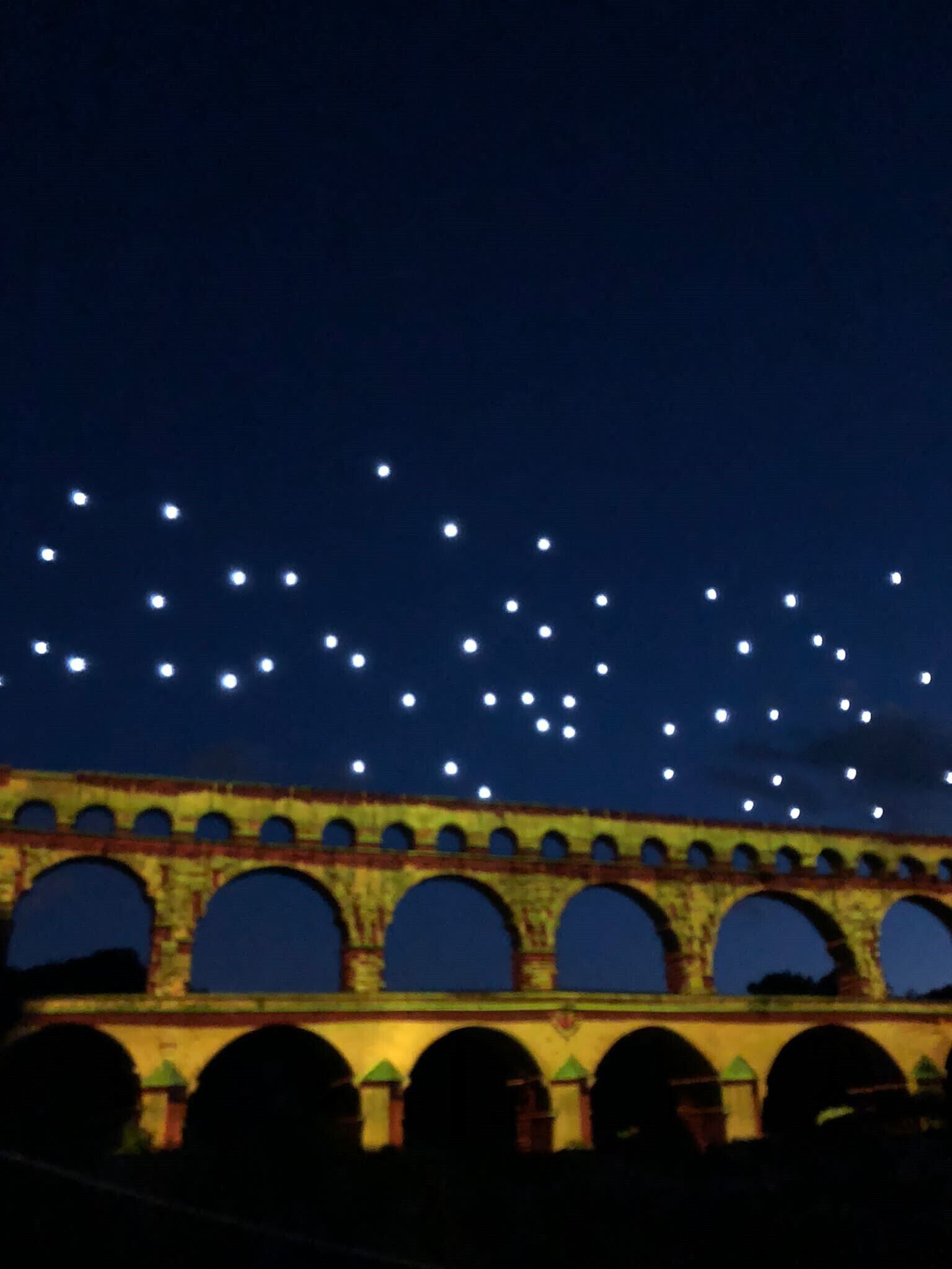Un pont à arcades multiples, illuminé par de nombreuses lumières, sous un ciel nocturne.
