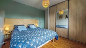 Een slaapkamer met een houten hoofdeinde, een bed met een blauw geborduurd beddengoed, een nachtkastje met een lamp, en een houten vloer.