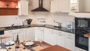 Een moderne keuken met witte kasten, een zwart fornuis en een eethoek met een houten tafel gedekt voor vier personen.