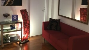 A living room with a red sofa, a glass coffee table, a decorative vase, a framed mirror, and a wall-mounted artwork. - DuomoSuite (Naples)