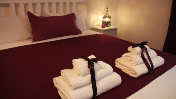 A neatly made bed with a red blanket, white pillows, and two stacks of folded towels with ribbons. - DuomoSuite (Naples)