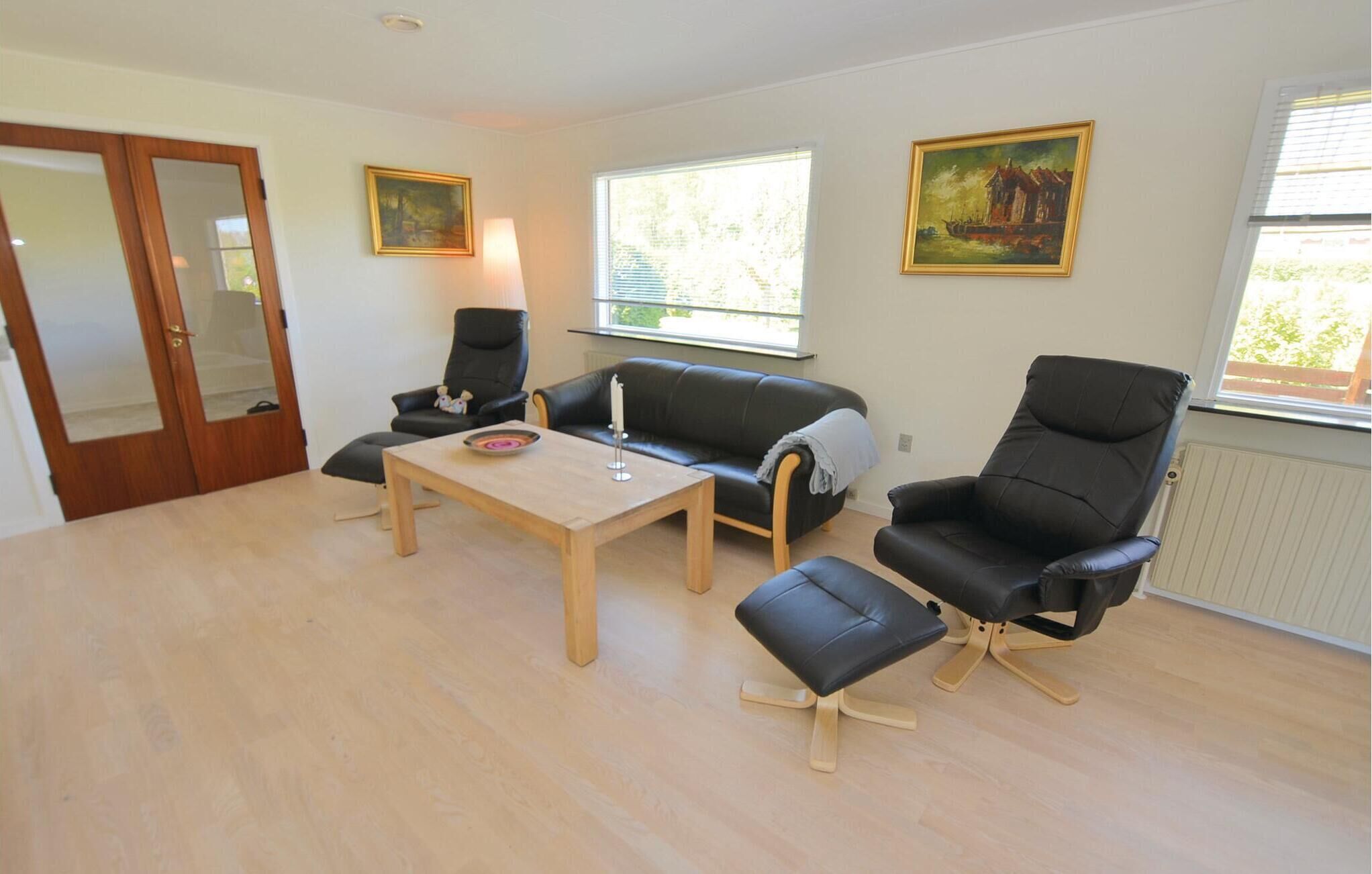 Uma sala de estar com uma mesa de centro de madeira, um sofá de couro preto, uma poltrona de couro preto e duas pinturas nas paredes.
