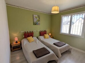 A room with two beds, a window, a lamp, and a painting on the wall. - Comfortable house, Denneville, 6 pax, near the sea (Denneville)