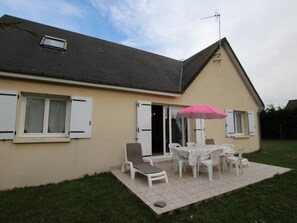 Une maison avec un patio, une table entourée de chaises et un parasol rose.