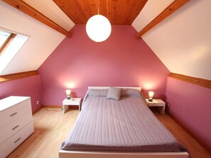 Une chambre avec un plafond en pente, un lit avec une tête de lit, des lampes de chevet et une commode.