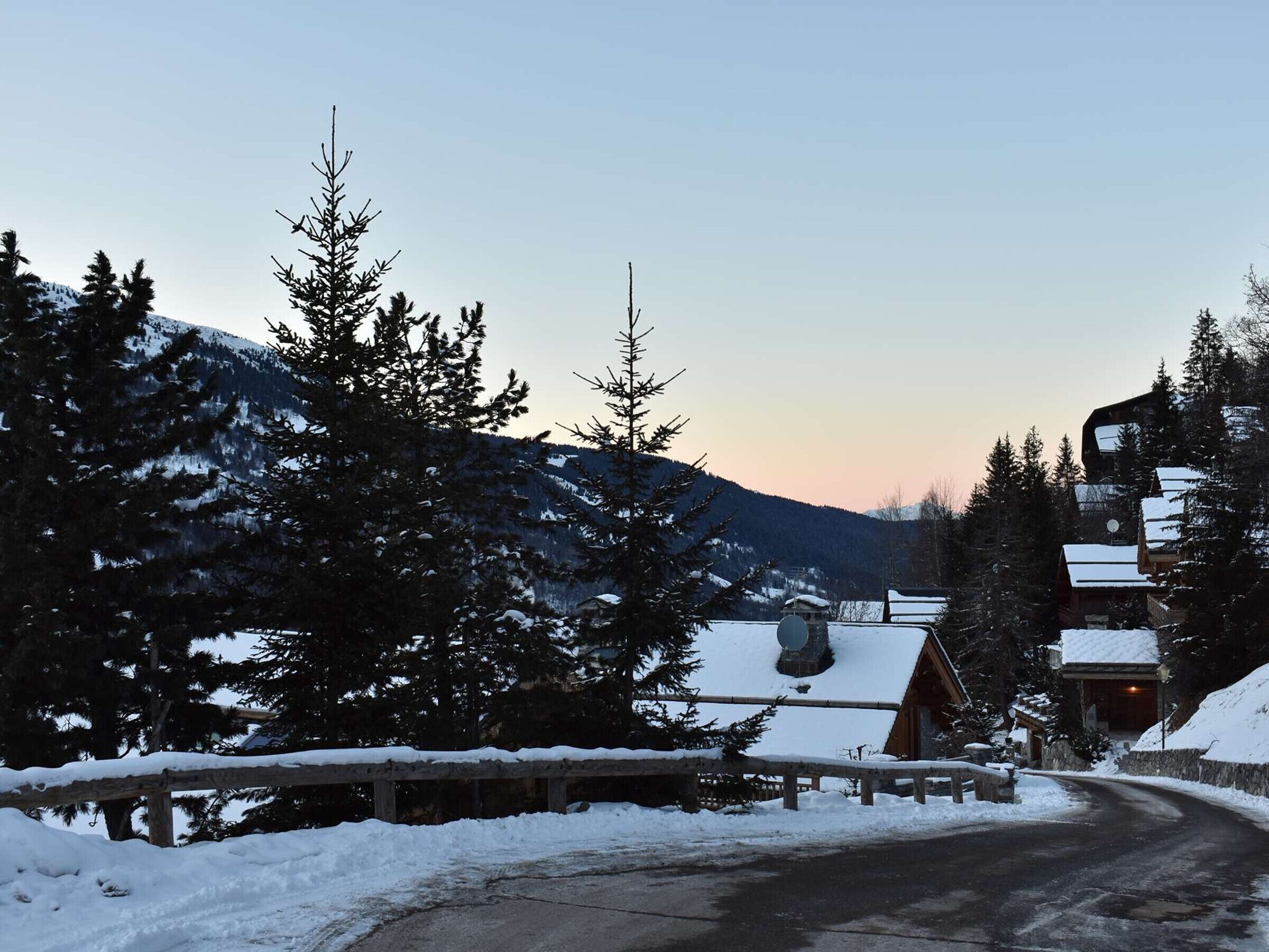Un paysage montagneux enneigé avec un chalet en bois et une route menant à ce chalet.