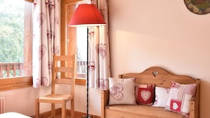 Una habitación acogedora con una silla de madera, un banco de madera con cojines, una lámpara roja de pie y una ventana con cortinas.