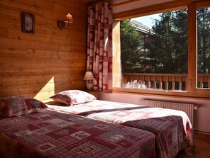Une pièce confortable avec deux lits, une fenêtre donnant sur les arbres, une lampe fixée au mur et une décoration en forme de cœur.