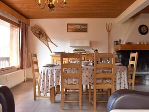 Un coin repas avec des chaises en bois et une table dressée pour quatre personnes, une cheminée et une horloge au mur.