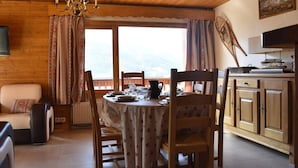 Un rincón comedor acogedor con una mesa de madera dispuesta para cuatro personas, rodeada de sillas. Un candelabro cuelga del techo, y una ventana ofrece vistas al exterior.