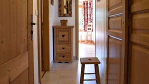 Un pasillo con puertas de madera y un taburete pequeño de madera. Se observa un armario de madera con recortes en forma de corazón y un espejo encima.