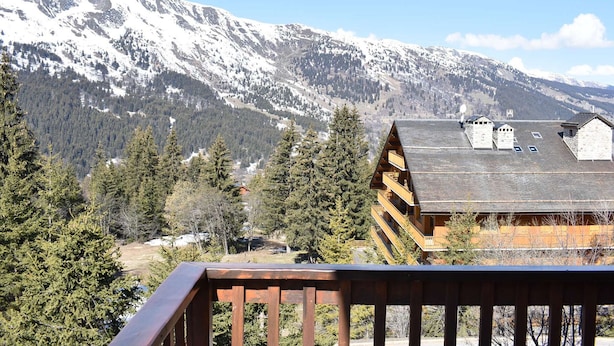 Un albergue de montaña con fachada de madera, varios balcones y vistas a montañas nevadas.