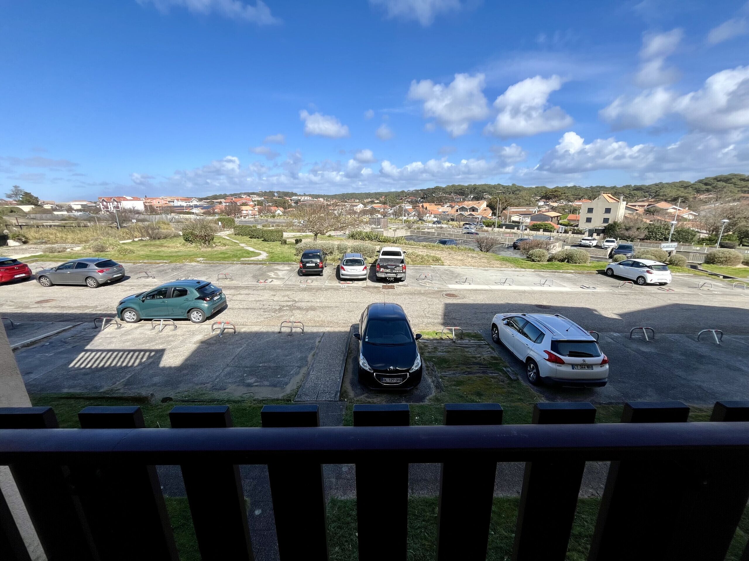 Een parkeerplaats met verschillende auto's, een heldere lucht en gebouwen op de achtergrond.