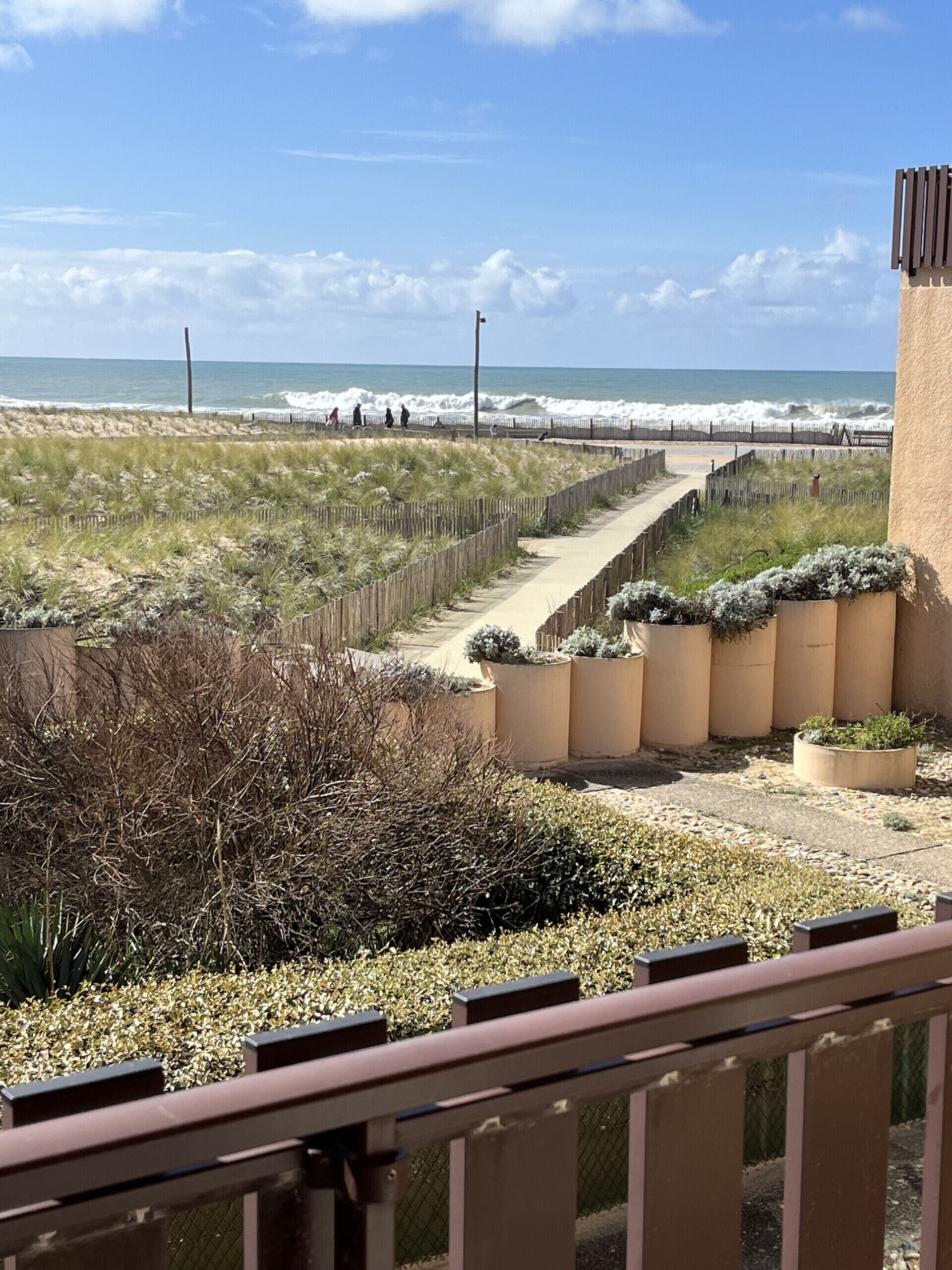 Un paseo marítimo con vistas al océano, un sendero de arena y una valla de madera.