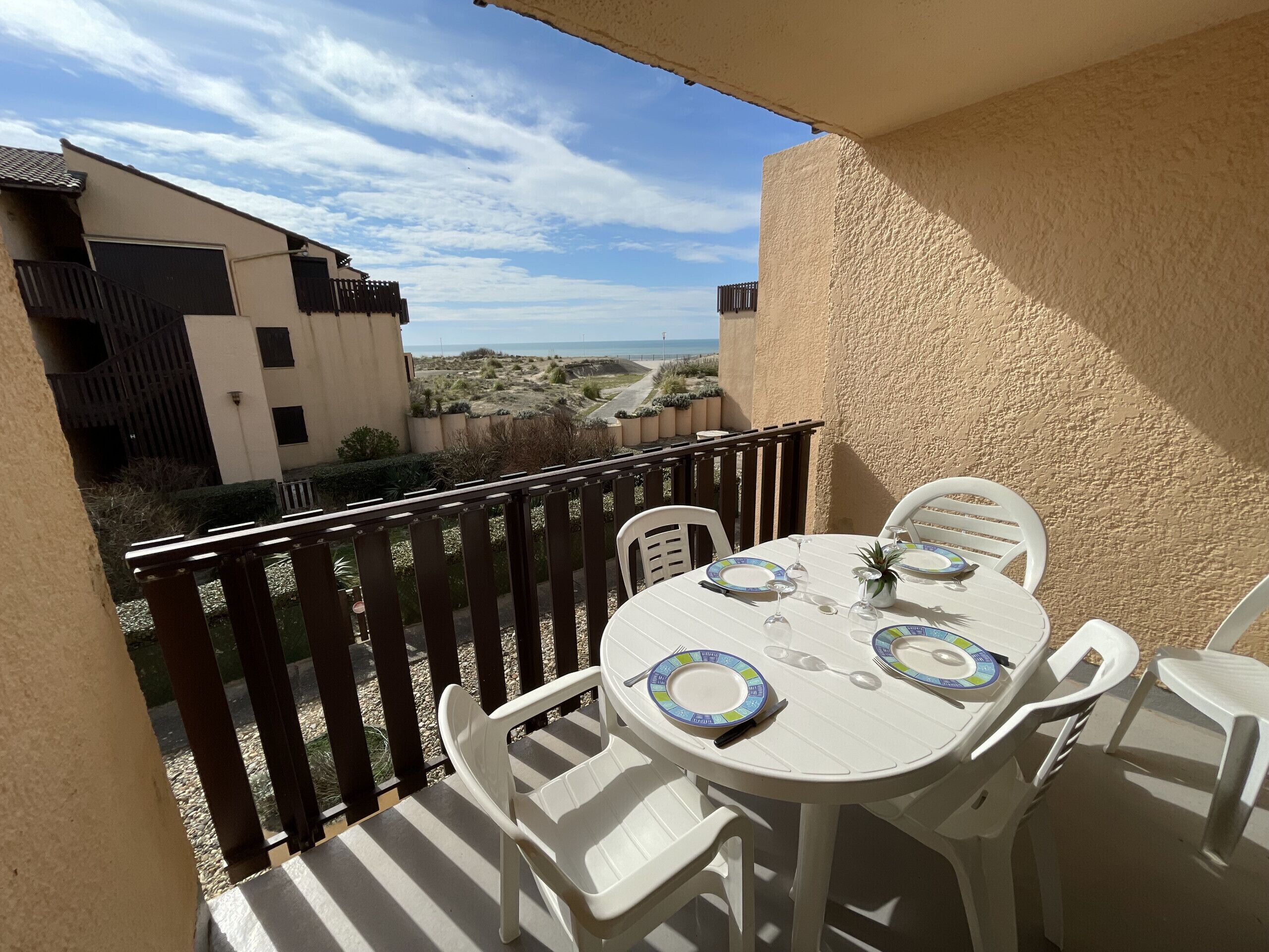 Uma varanda com uma mesa posta para dois, cadeiras brancas e vista para a praia.