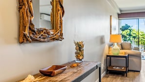 A wooden console table with a mirror, a bowl, and a vase with dried flowers. A lamp and a sofa are visible in the background. - GORGEOUS REMODEL-WELL EQUIPPED-MODERN LUXURY-AC THROUGHOUT (Kihei)