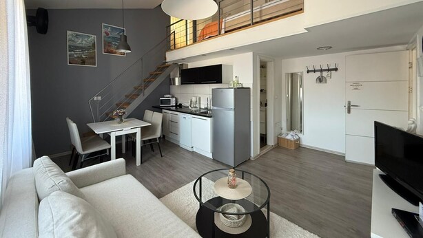 Un apartamento moderno con comedor, cocina, sala de estar y una escalera a un nivel superior.
