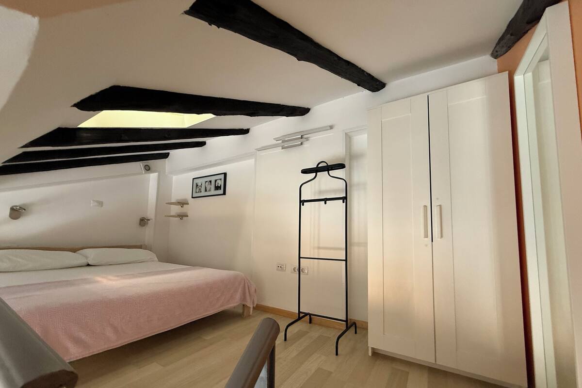 A bedroom with a bed, a wardrobe, a coat rack, and a skylight.