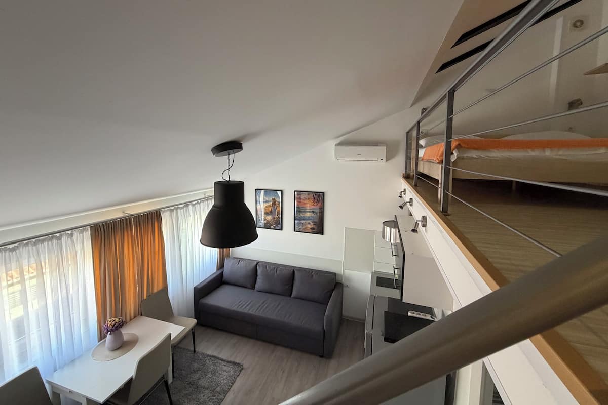 A modern apartment with a dining area, a sofa, a staircase, and a bunk bed.