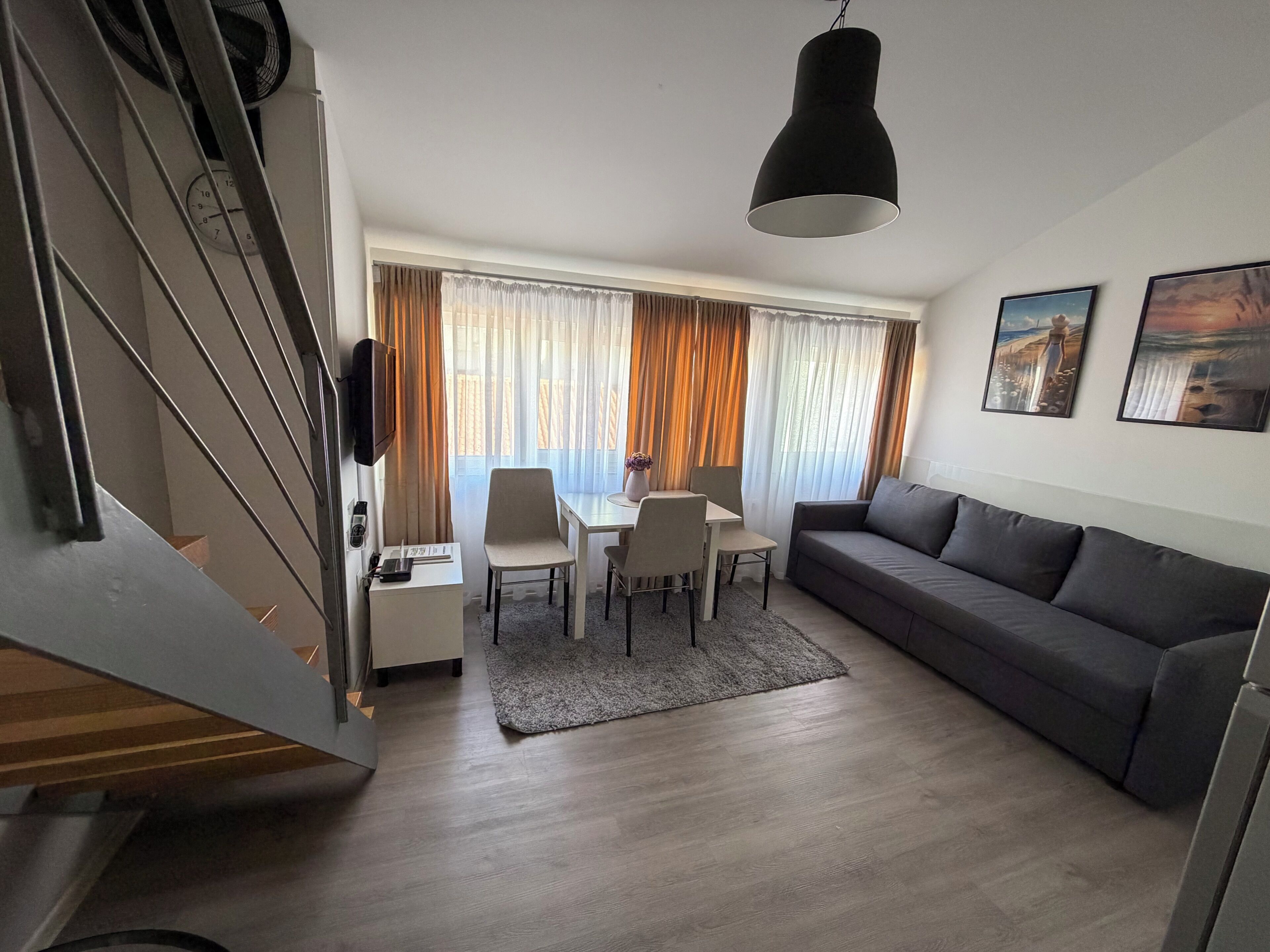 A modern living room with a sofa, dining table, chairs, and a staircase.