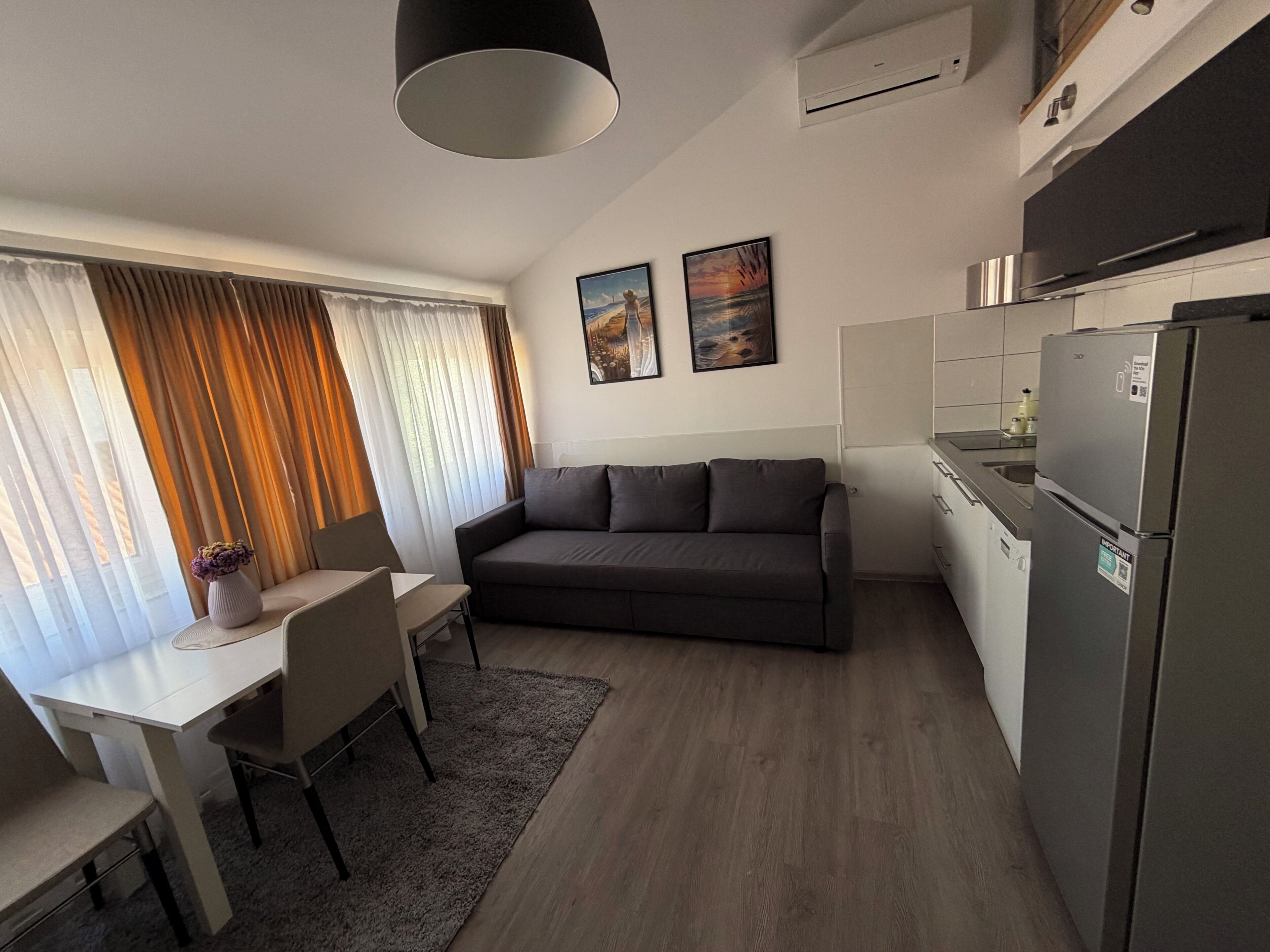 A modern kitchen with a refrigerator, a dining area with a table and chairs, and a sofa.