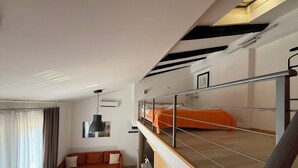 Un apartamento moderno con un entrepiso que funciona como dormitorio, una sala de estar con sofá, una mesa de comedor y un balcón con barandilla.
