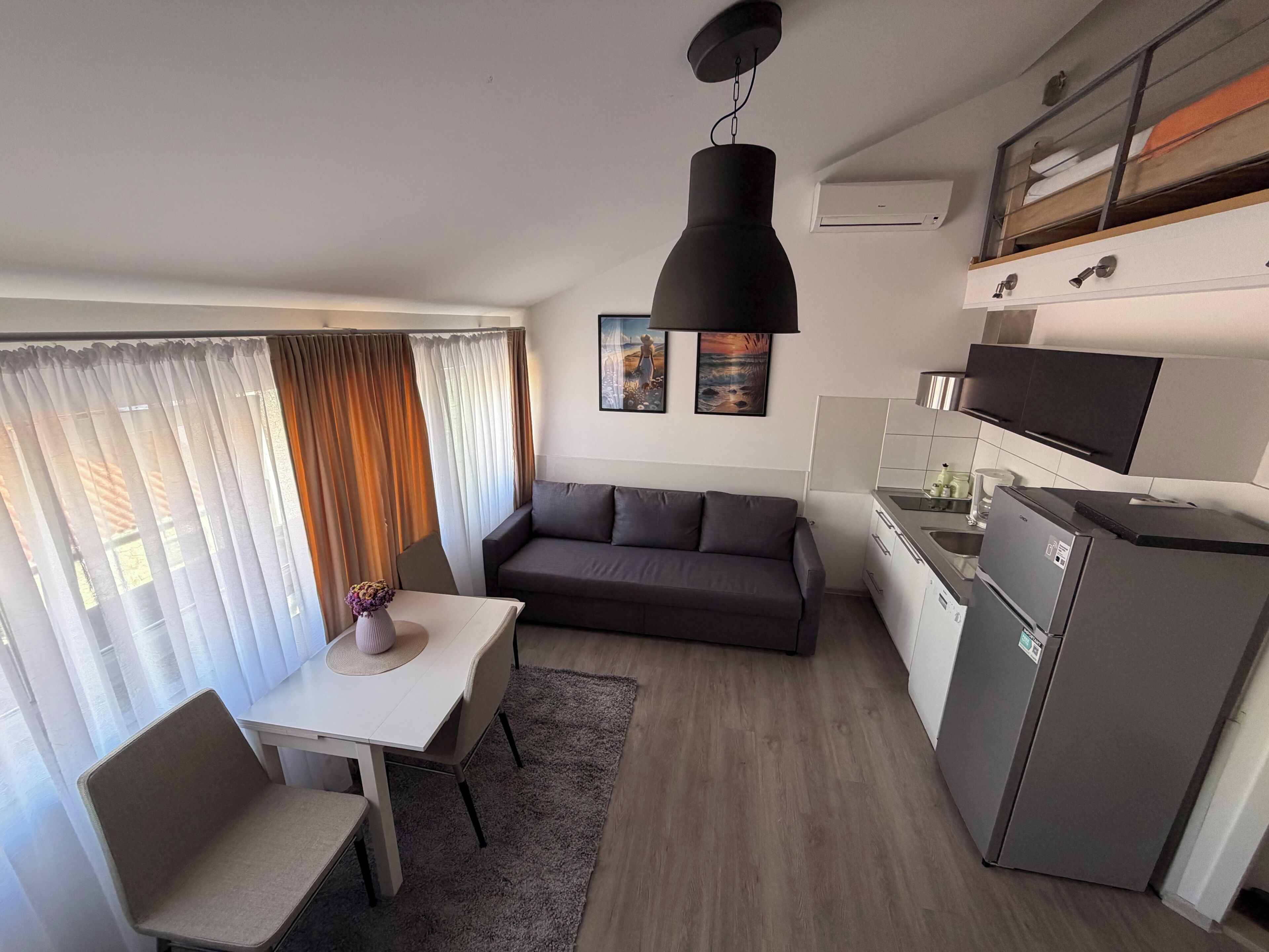 A compact living space with a dining area, sofa, kitchenette, and a ceiling light fixture.