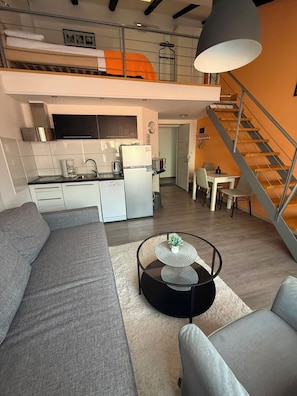 Un apartamento moderno con un dormitorio en entrepiso, cocina, comedor y escalera.