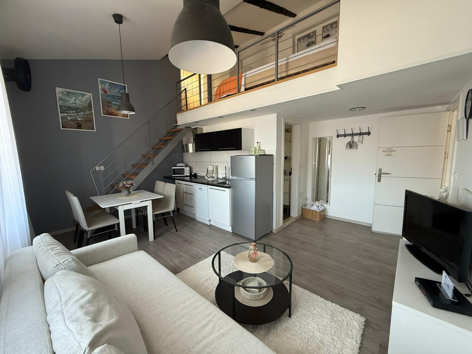 A modern apartment with a living room, dining area, kitchen, and a staircase to an upper level.