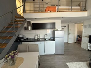 Cocina moderna equipada con lavavajillas, microondas y cafetera. Hay un comedor con mesa y sillas, y una escalera que lleva a un nivel superior.