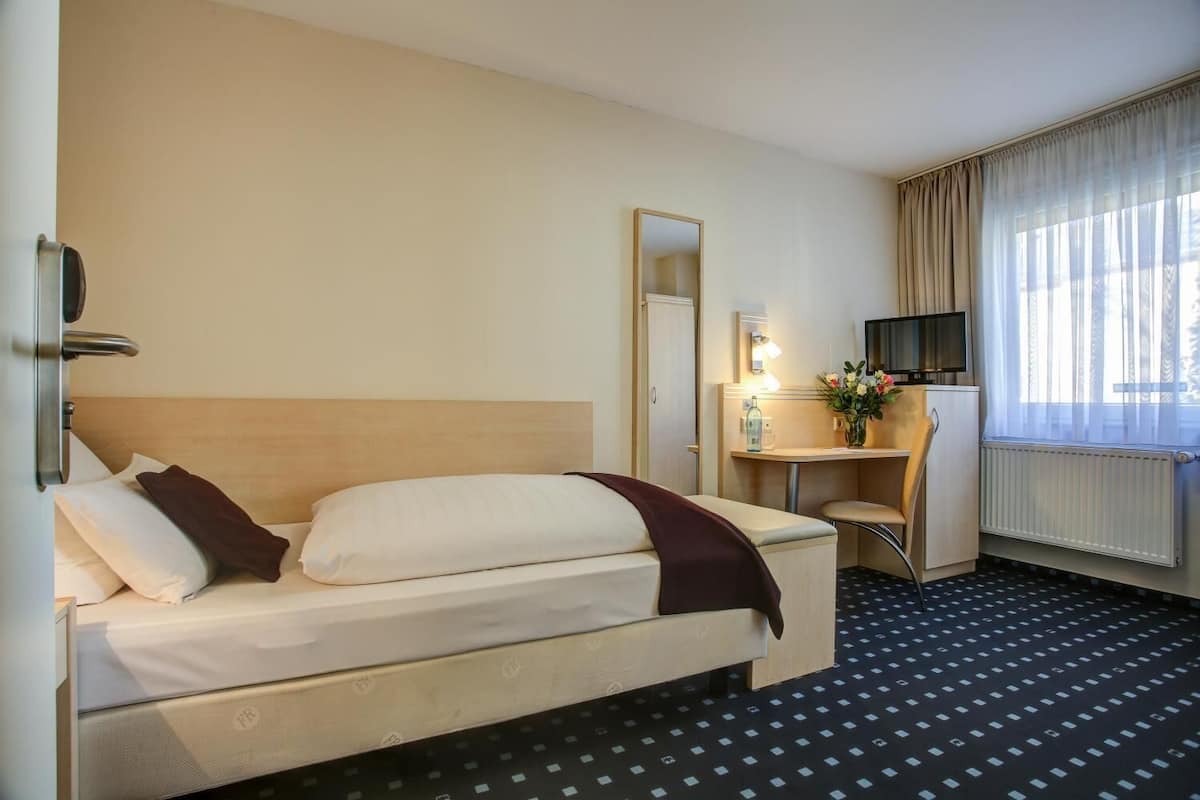 A hotel room with a bed, a desk, a mirror, a TV, and a window with curtains.
