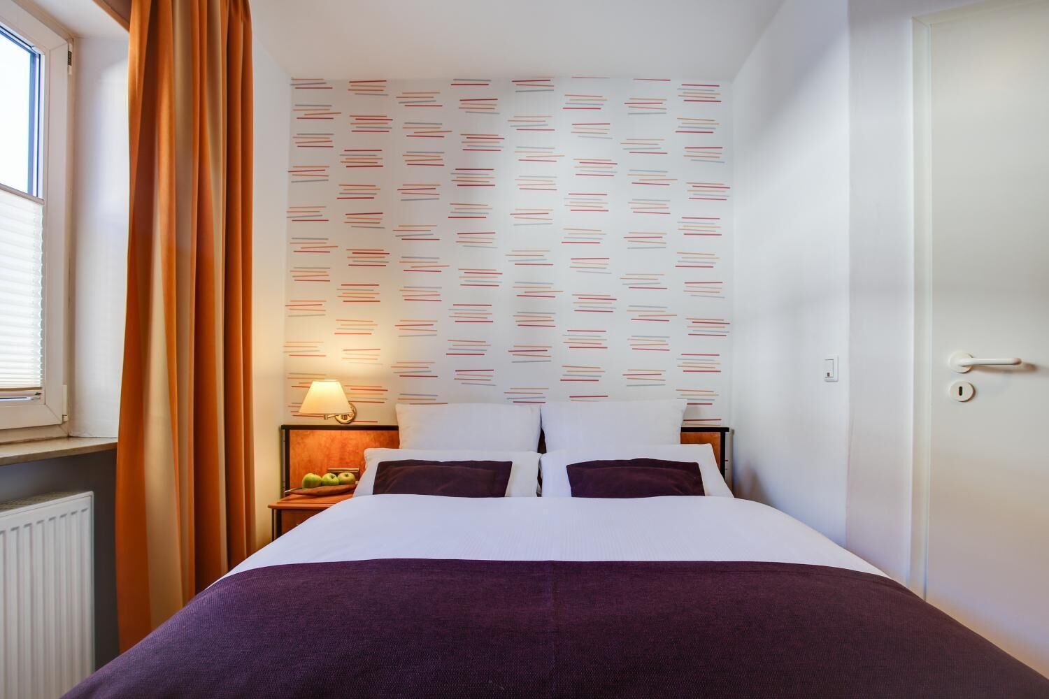 A hotel room with a bed, a nightstand with a lamp, and a window with curtains.