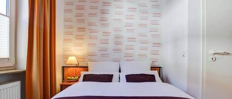 A hotel room with a bed, a nightstand with a lamp, and a window with curtains.