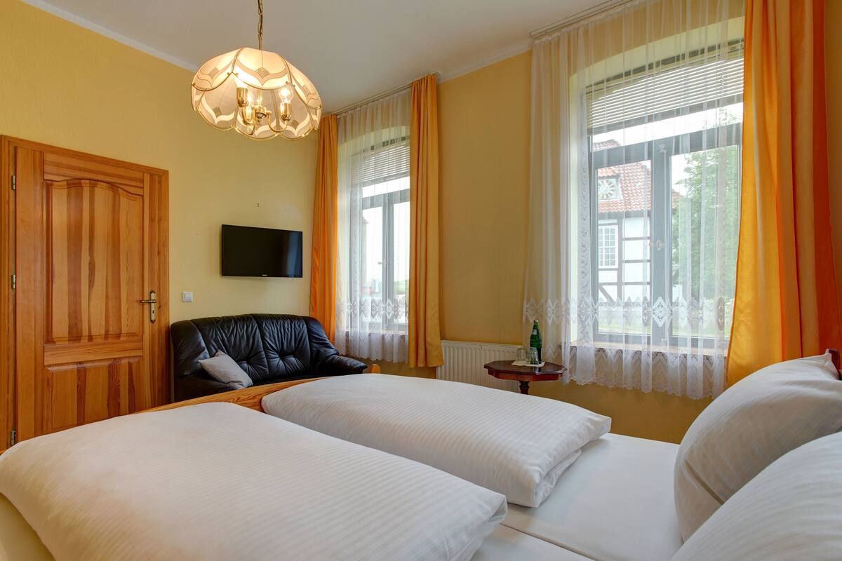 A hotel room with two beds, a television, a wooden wardrobe, and a window with curtains.